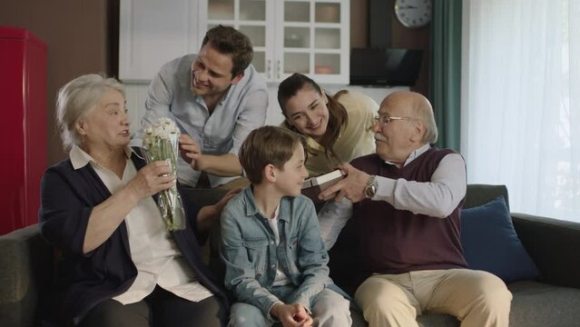 Happy family portrait.A scene where a young couple gives flowers and a gift box to their elderly parents. The extended family celebrates a birthday, holiday, mother's day or father's day.