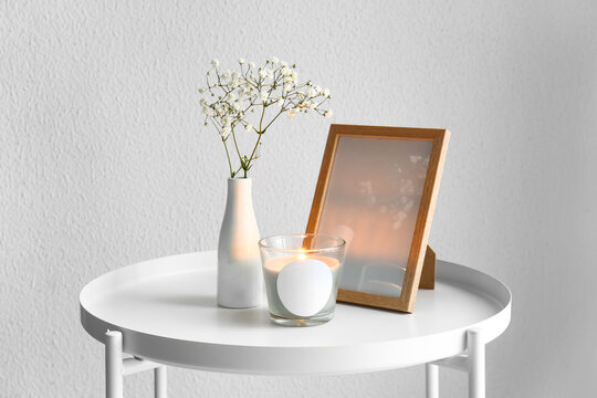 Holder with burning candle, photo frame and flowers on table in room