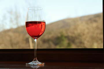 Glass of red wine stands on wooden windowsill