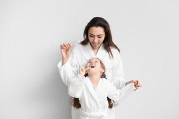 Little girl with her mother brushing teeth on light background