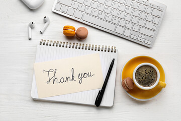 Notebook with text THANK YOU, macaroons, earphones, computer keyboard and cup of coffee on white wooden background