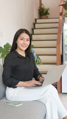 Pretty Asian woman using laptop for surfing internet or watching movie on sofa.