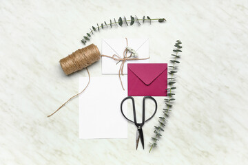 Envelopes with blank card, eucalyptus branches, scissors and rope on white background