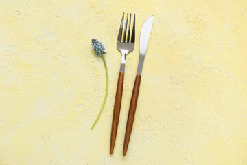 Silver fork, knife and Muscari flower on yellow background
