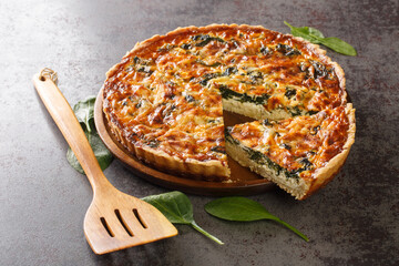 Savory tart of rich egg custard, spinach and cheese with cut out a slice on the plate on the gray table close-up. Hotizontal