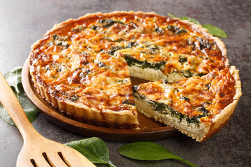 Quiche Florentine with spinach, cheese, eggs and spices on gray table with spatula, close-up. Hotizontal
