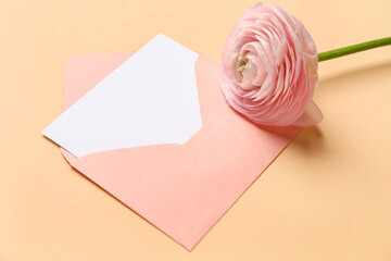 Envelope with blank card and pink ranunculus flower on beige background