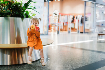 Toddler girl eats donut in supermarket on bench, snack with pastries shopping. Cute child girl in...