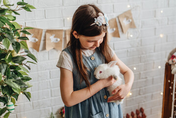 A girl hugs a cute white rabbit at home. A girl with a rabbit, a pet rabbit. A girl cuddles a white rabbit in the studio.