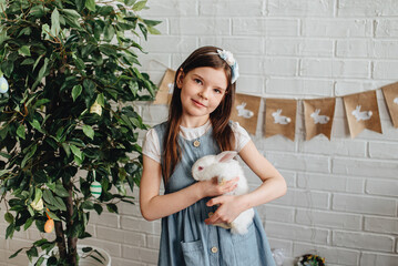 A girl with freckles hugs a cute white rabbit at home. A girl with a rabbit, a pet rabbit. A girl cuddles a white rabbit in the studio.
