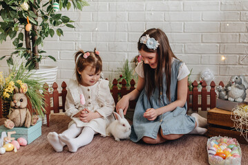 Two girls are playing with a white rabbit on the floor of the house.