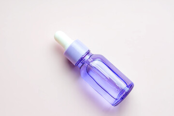 purple dropper bottle with essential oil or face serum on beige background. Daily routine treatment for young skin