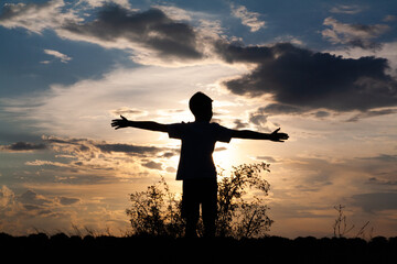 The boy spread his arms out to the sides and enjoys the view of the magical sunset