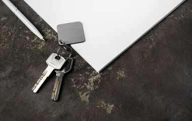 Real estate agency concept. Keys, blank keychain, pen and paper on concrete background.