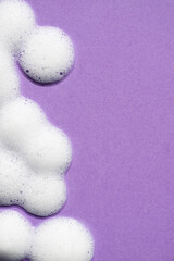 Foam swatch on a purple background. Soapy liquid texture with bubbles. Natural sunshine and shadows. Skin care cleansing cosmetic in top view.