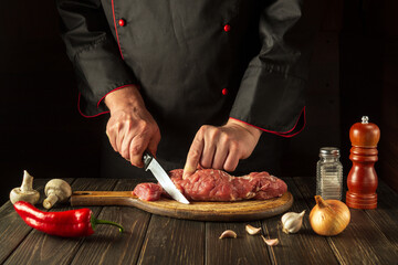 The cook cuts raw beef meat on a cutting board before baking. Asian cuisine. Hotel menu recipe idea.