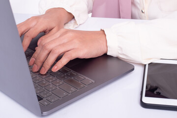 Cropped image of woman hand typing on laptop in office with mobile phone. Working concept.