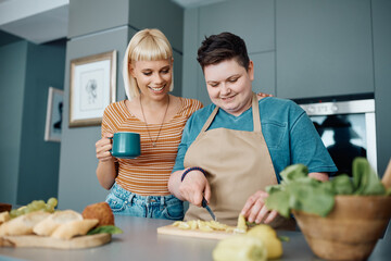 Happy homosexual women preparing meal in kitchen at home.