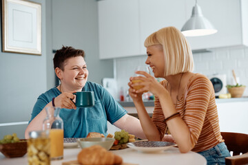 Happy gay women enjoying in conversation during breakfast at dining table.