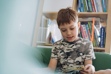 Little caucasian boy reading a book sitting on couch