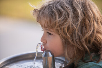 Child drinking water from a water fountain in park outdoor.