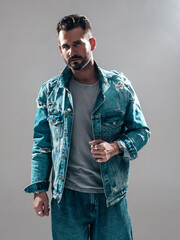 Portrait of handsome confident stylish hipster lambersexual model. Sexy man dressed in jeans jacket. Fashion male isolated on grey background in studio