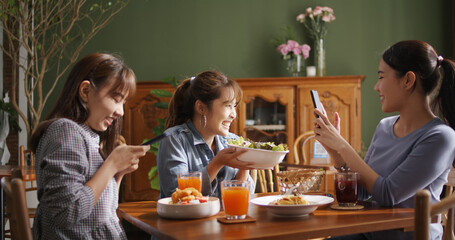 Small girl group party asia people busy talk smile eat brunch food drink. Young woman fun happy hour meal shoot photo of dish plate salad bowl on table post ig reel story app in vegan cafe bar shop.
