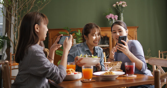 Small girl group party asia people busy talk smile eat brunch food drink. Young woman fun happy hour meal shoot photo of dish plate salad bowl on table post ig reel story app in vegan cafe bar shop.