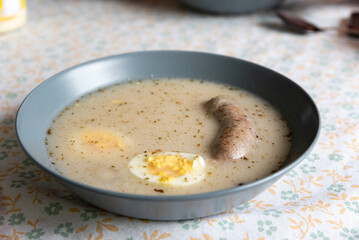 Easter sour rye soup with white sausage and egg. Traditional Polish dish for Easter. Sour rye soup in a plate and on a tablecloth with patterns.