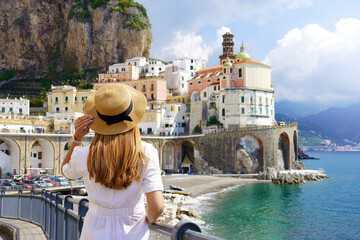 Fototapeta na wymiar Holiday in Italy. Back view of young woman with white dress and hat looking the village of Atrani on Amalfi Coast, Italy.