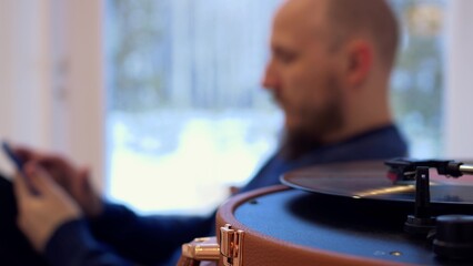 A vinyl record is spinning in the player, in the background an unrecognizable man is listening to classical music alone in the background. Ventage listening to music.