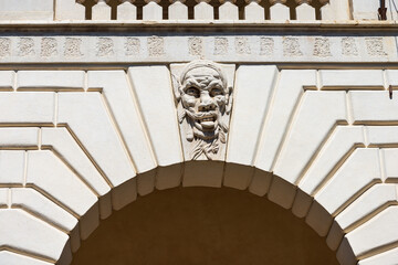 Fototapeta premium Brescia. Closeup of Medieval Broletto Palace (Palazzo Broletto or Palazzo del Governo), XII-XXI century. White stone arch with keystone and a gargoyle grotesque human mask. Lombardy, Italy, Europe.