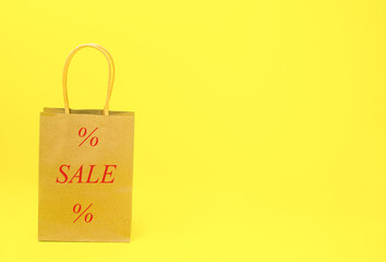 Fototapeta na wymiar Paper bag with the inscription SALE WITH PERCENT on a yellow background. The concept of sale, online, shopping, business, shop, discounts, gifts. High quality photo