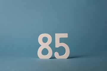 White wooden number eighty-five 85 on blue background.