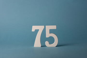 White wooden number seventy-five 75 on blue background.