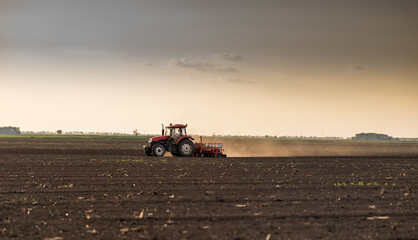 Fototapeta premium Farmer with tractor seeding - sowing crops at agricultural field