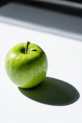 close up of green apple with shadow on white.