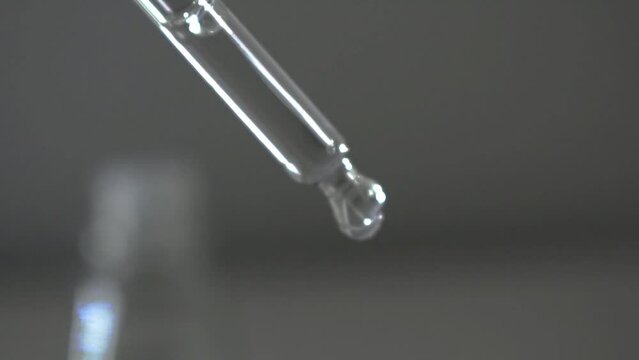 Glass transparent pipette dropper for medical, cosmetic, scientific biology and chemistry laboratory procedures being used by industry professional by dripping liquid water solution droplet 