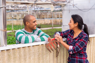 Hispanic male farmer talks to a female colleague in the farmyard, discussing interesting topics during a break..from work.
