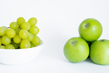 green grapes in bowl near apples on white.