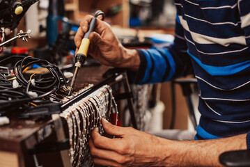 Industrial worker man soldering cables of manufacturing equipment in a factory. Selective focus