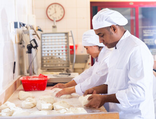 Professional hispanic baker standing at work table, kneading and forming dough for baking bread