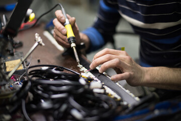 Industrial worker man soldering cables of manufacturing equipment in a factory. Selective focus