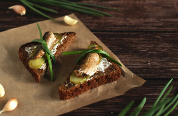 brown bread sandwiches with pickles, onions, garlic and sprats on a wooden background