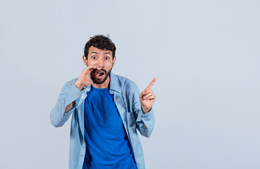 Fototapeta premium Handsome man whispering and pointing to the side, guy whispering and pointing fingers to the side, latin guy pointing at blank space