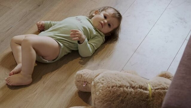 Baby girl lying on her back on the floor next to her teddy bear getting up and starting to crawl. Baby care. Family care.