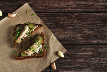 brown bread sandwiches with pickles, onions, garlic and sprats on a wooden background