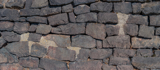 Panoramic view over a long middle age stone wall with patterns of ancient bricks and stones as a background, closeup, details.