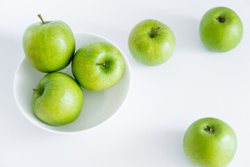 top view of green and juicy apples in bowl on white.