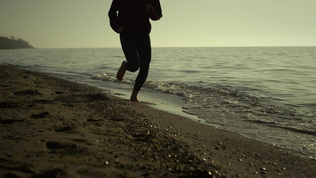 Unknown girl jogging sandy beach. Slim woman legs running at sunset outside. 